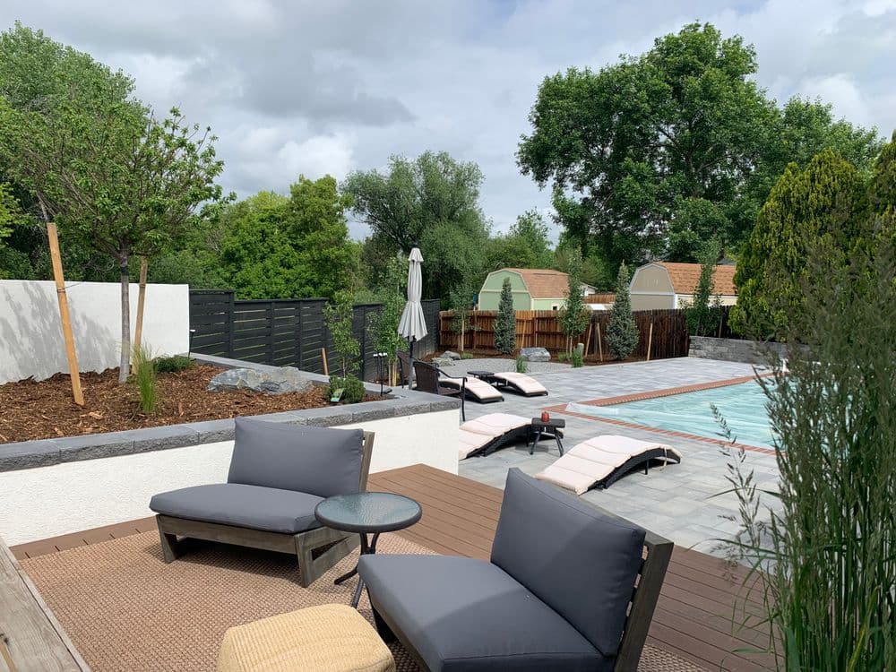 Modern outdoor pool area with lounge chairs, greenery, and shaded seating. Relaxing summer retreat.