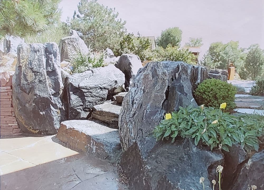 Scenic garden pathway with large rocks, greenery, and yellow flowers nestled among the stones.