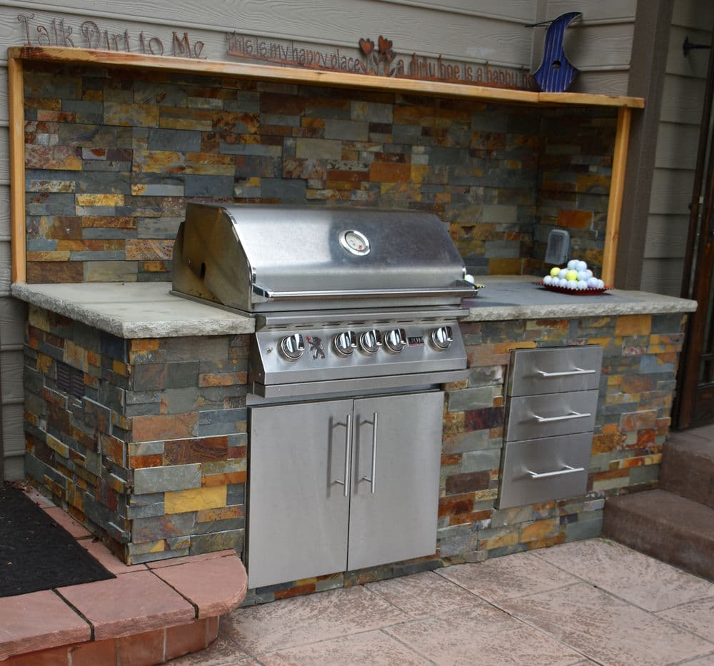 Outdoor stone kitchen featuring a stainless steel grill, countertops, and storage drawers.