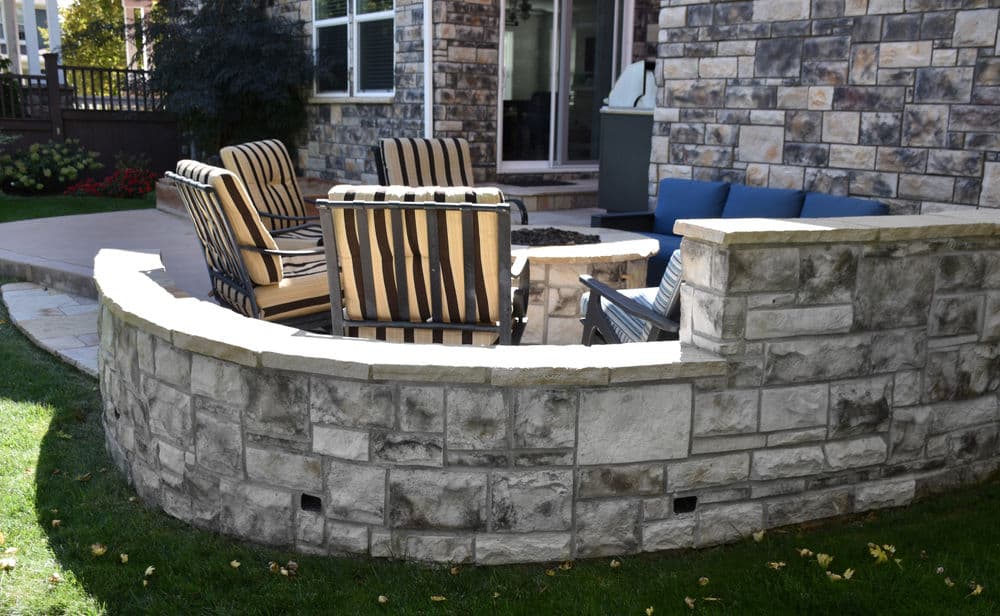 Stylish outdoor seating area with stone wall and cozy chairs, perfect for relaxation.