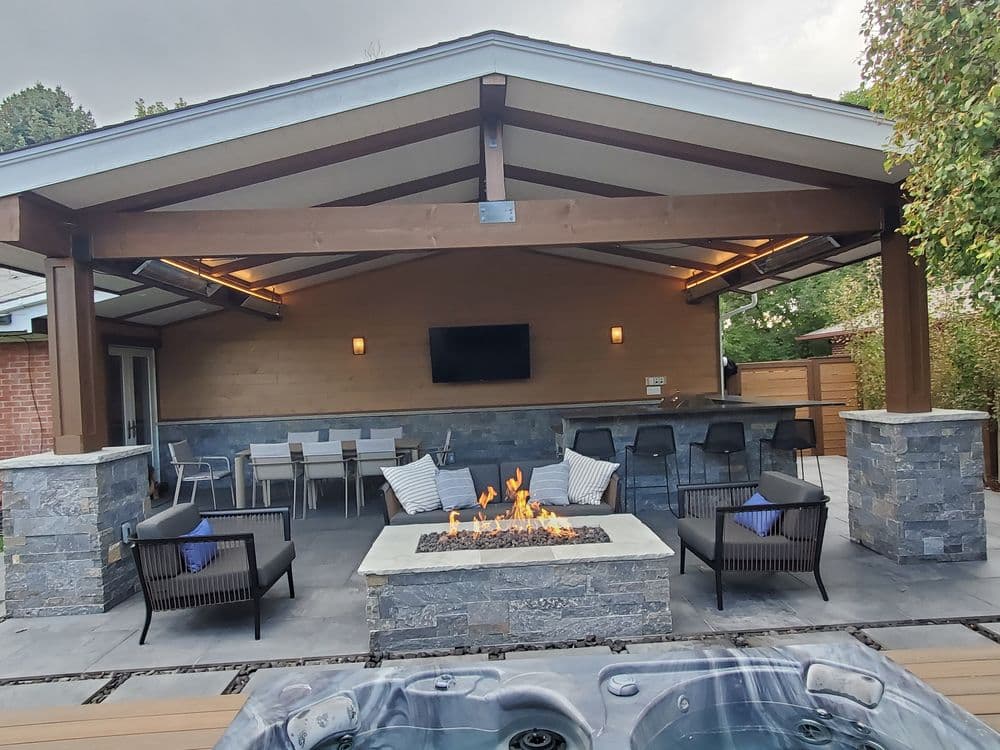 Modern outdoor patio with fireplace, seating area, and bar under a stylish roof.