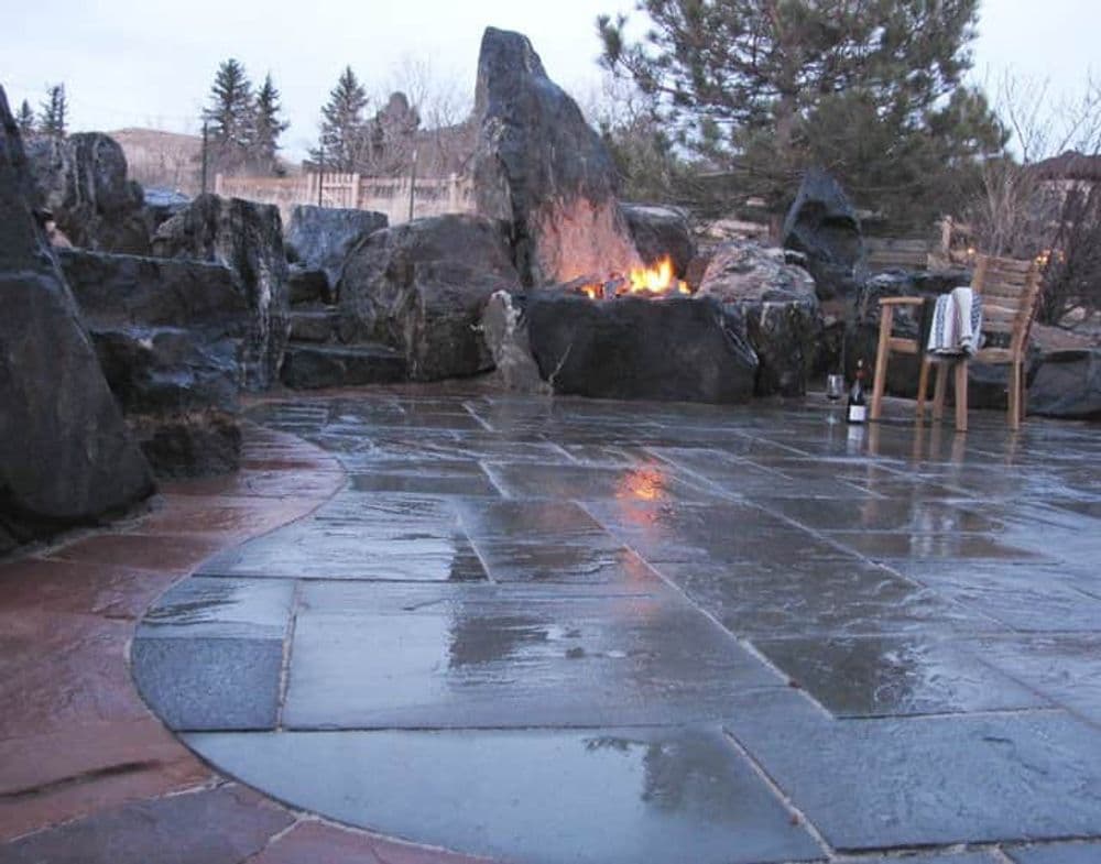 Outdoor stone patio with a fire pit surrounded by large rocks and a wooden chair.