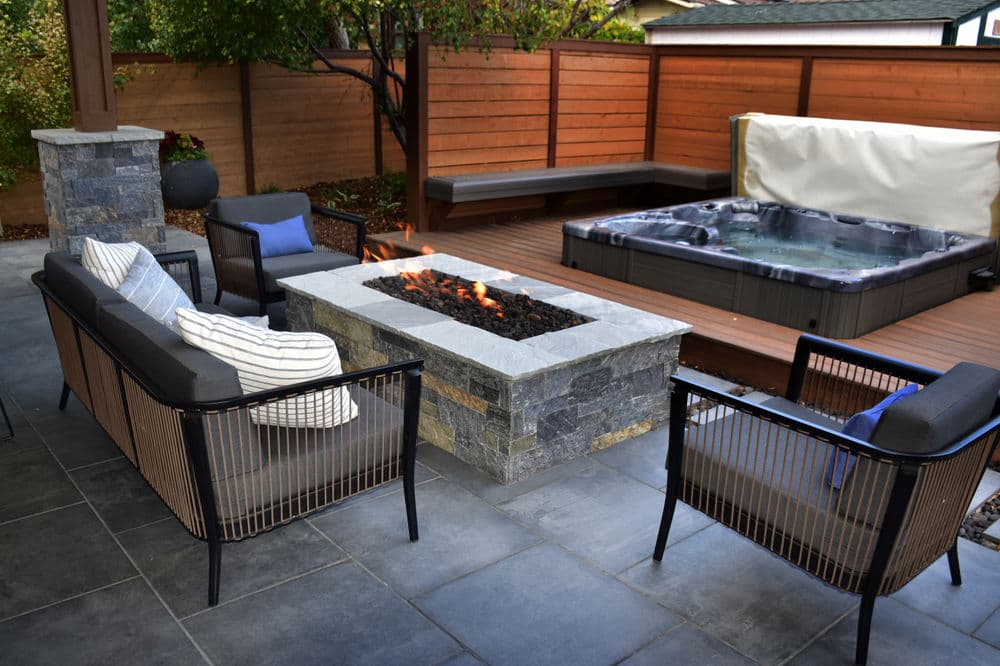 Cozy outdoor seating area with fire pit, hot tub, and wooden privacy fence. Ideal for relaxation.