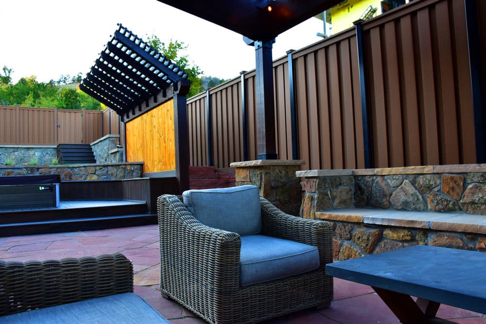 Cozy outdoor patio with wicker furniture, stone walls, and wooden fence, ideal for relaxation.