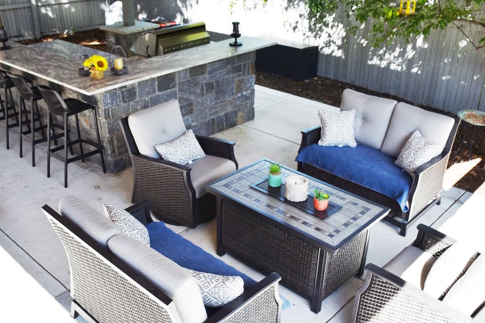 Outdoor seating area featuring wicker furniture, a stone table, and a modern grill setup.