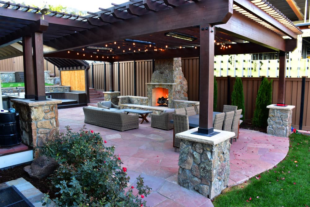 Cozy outdoor living space with fireplace, stone walls, seating, and string lights.