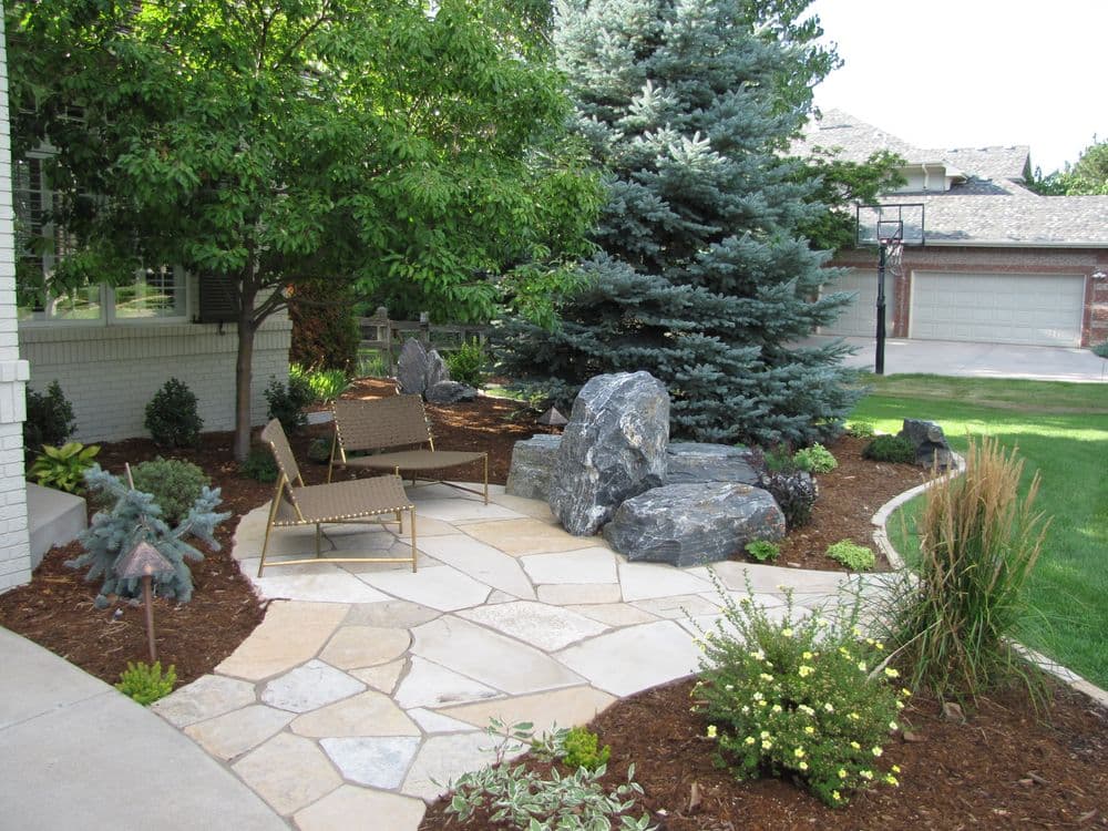 Landscaped garden with stone pathway, lounge chairs, and evergreen trees.