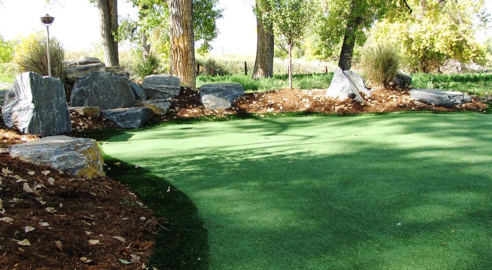 Lush green artificial turf landscape with stones and trees, perfect for outdoor relaxation.