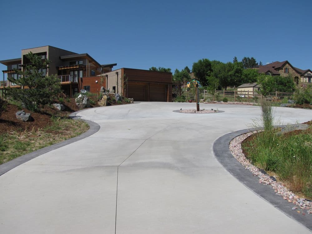 Modern house with curved driveway and landscaped garden in a sunny outdoor setting.