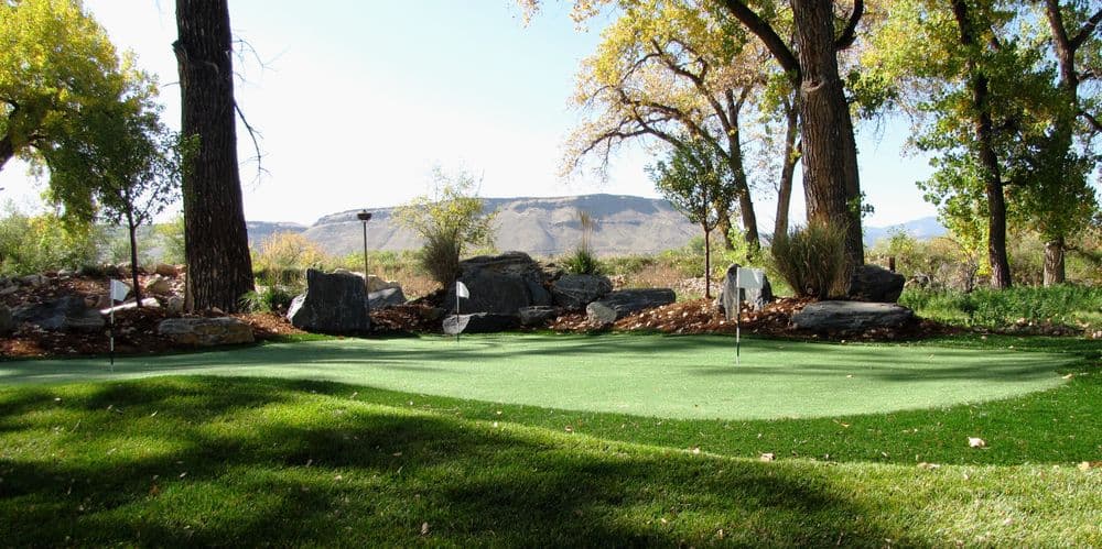 Lush green golf putting green with stone accents and mountain views in the background.