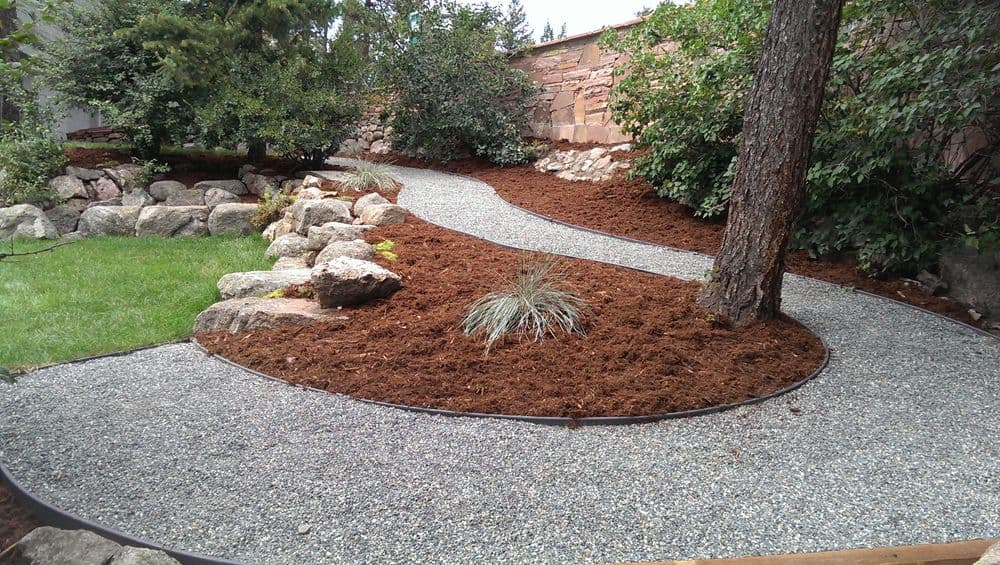 Winding gravel pathway through landscaped garden with rocks and trees.