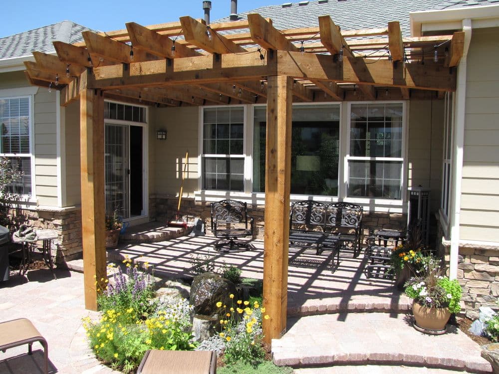 Wooden pergola over a patio, framed by flowers and seating, enhancing outdoor living space.