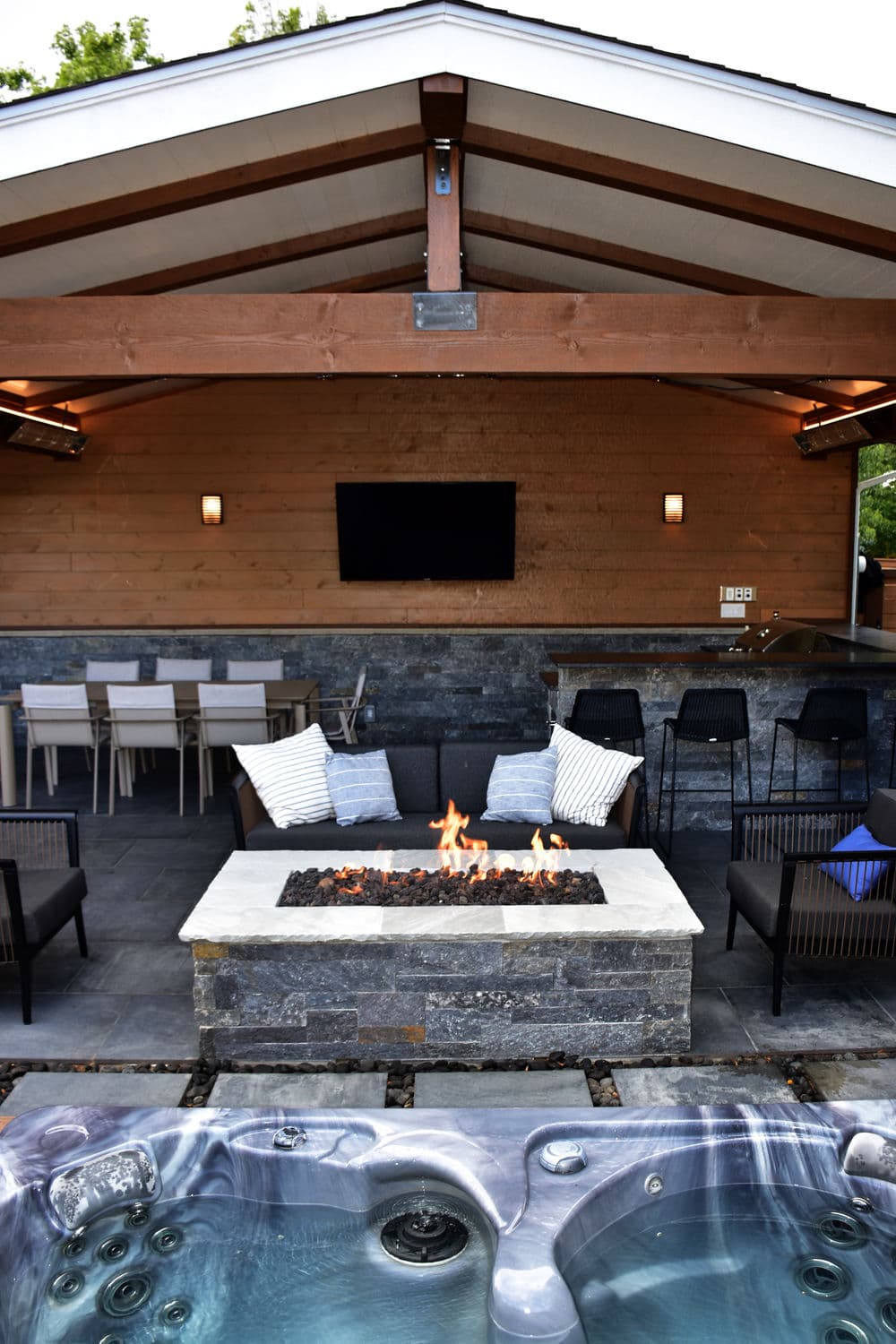 Modern outdoor patio with hot tub, fire pit, and dining area, perfect for entertaining.