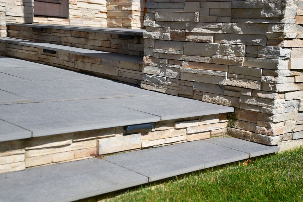 Modern stone steps and textured wall leading to an entrance, surrounded by greenery.