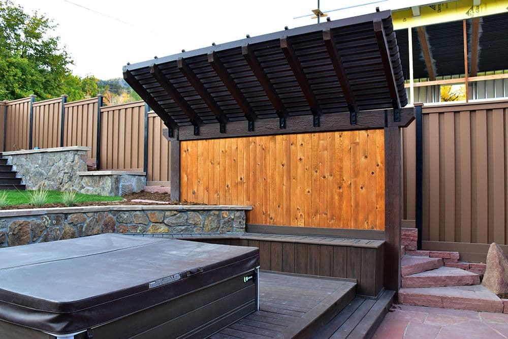 Modern outdoor hot tub with wood paneling and slatted roof in a landscaped backyard.