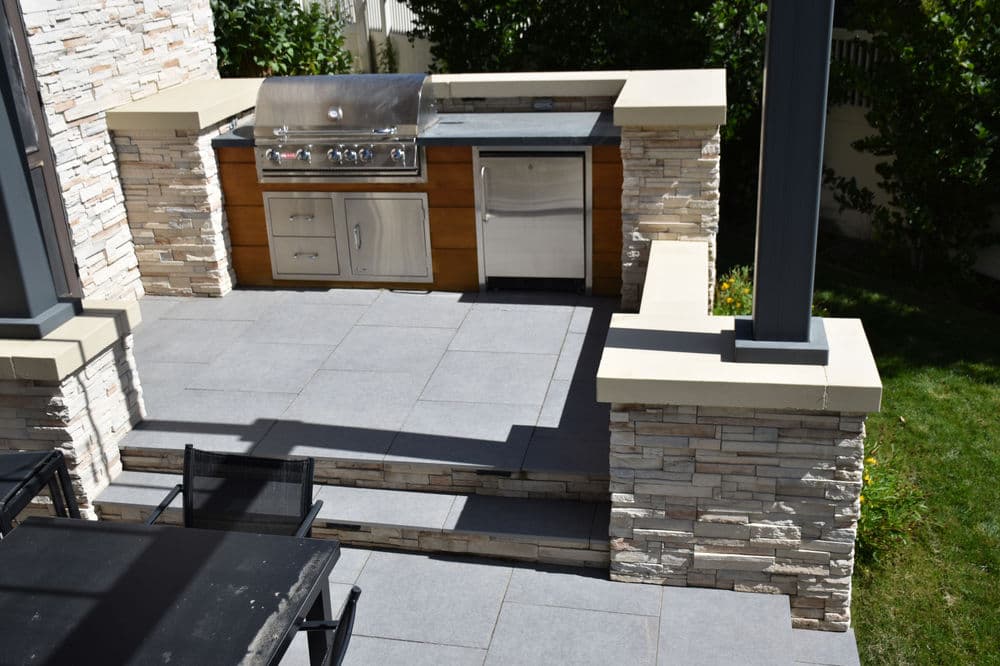 Outdoor kitchen with modern grill, stainless steel appliances, and stone accents. Modern patio design.
