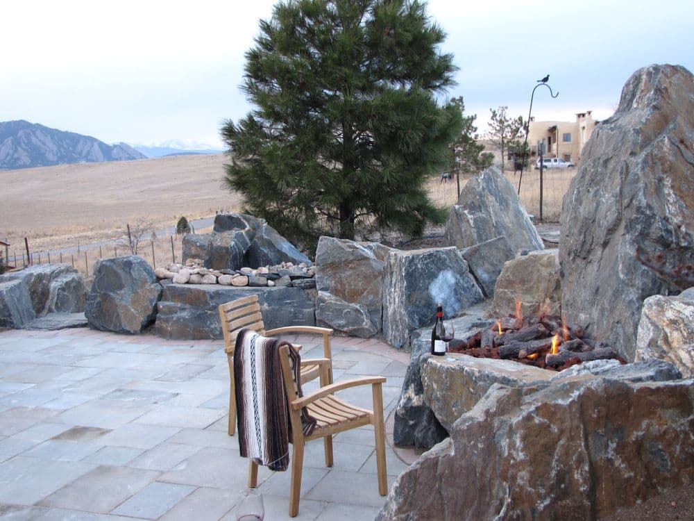 Outdoor patio with rock features, fire pit, wooden chairs, and a scenic mountain backdrop.