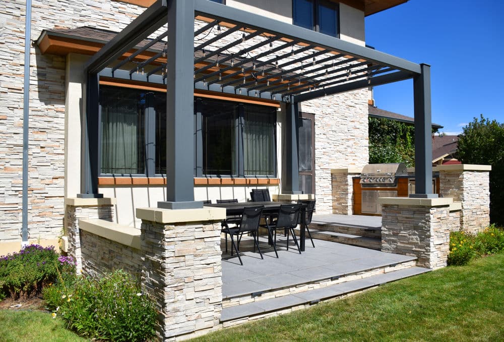 Modern outdoor patio with stone features, dining table, and grill under a pergola.
