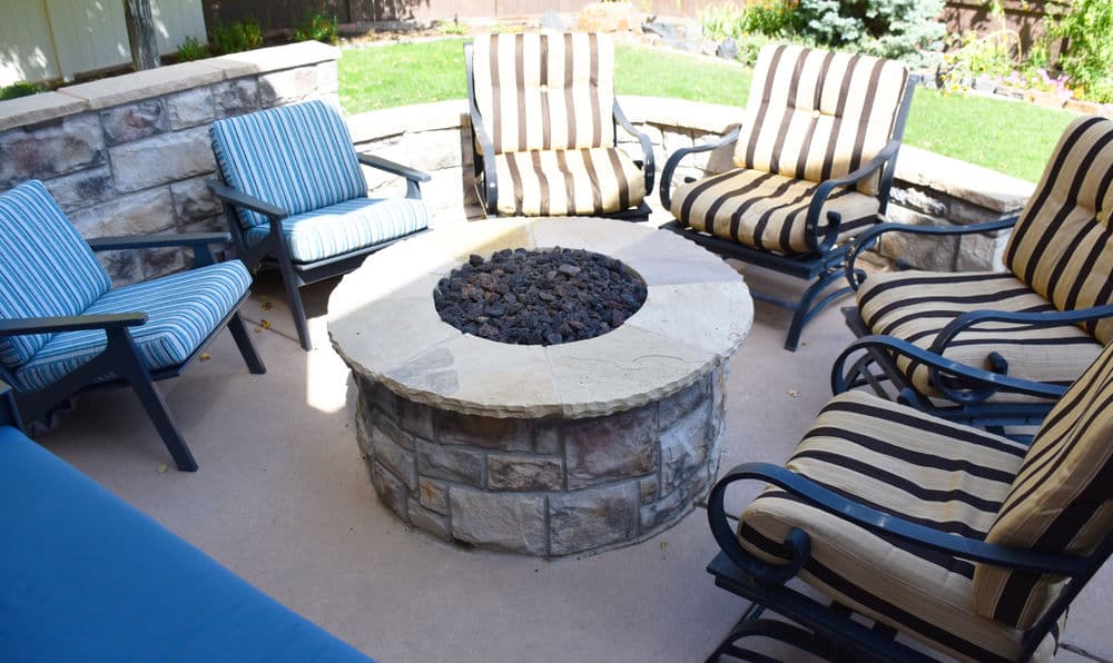 Cozy outdoor fire pit surrounded by striped lounge chairs in a landscaped backyard.