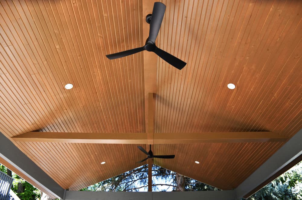 Modern wooden ceiling with two ceiling fans and recessed lighting in a spacious patio area.