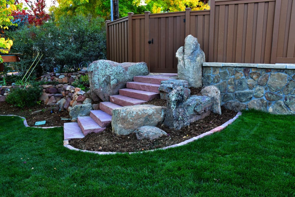 Stone steps leading to a garden, surrounded by landscaping and a wooden fence.