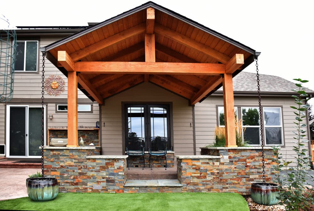 Modern home entrance with a wooden awning, stone accents, and lush green landscaping.