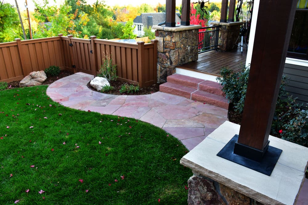Landscaped stone pathway leading to a deck in a vibrant backyard garden.